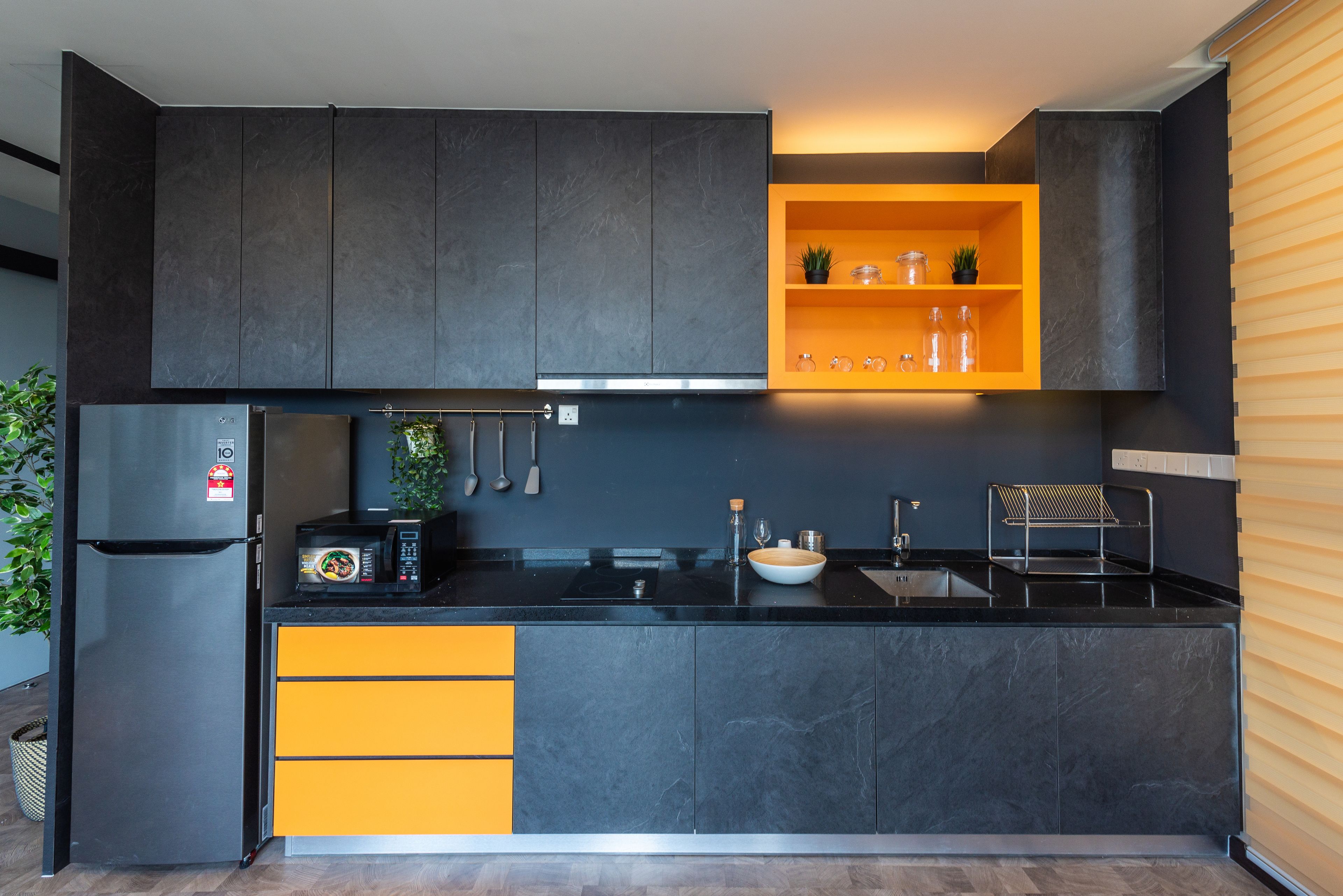 Une cuisine moderne avec des meubles de couleur sombre, un plan de travail noir et une étagère d’accent orange vif.