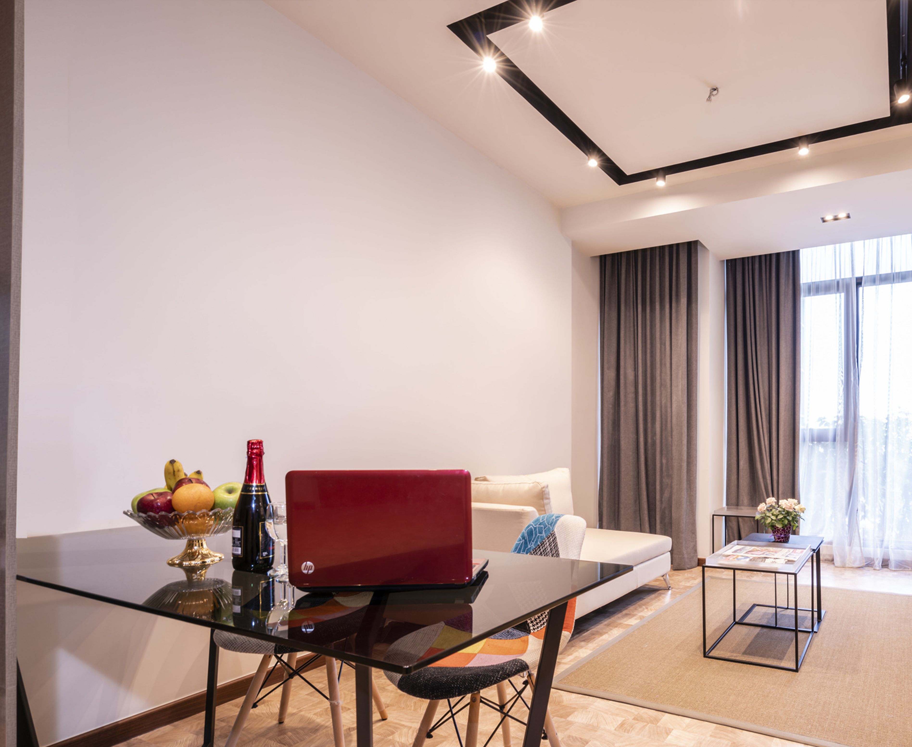 Un salón moderno con una mesa de vidrio, una computadora portátil y un frutero.