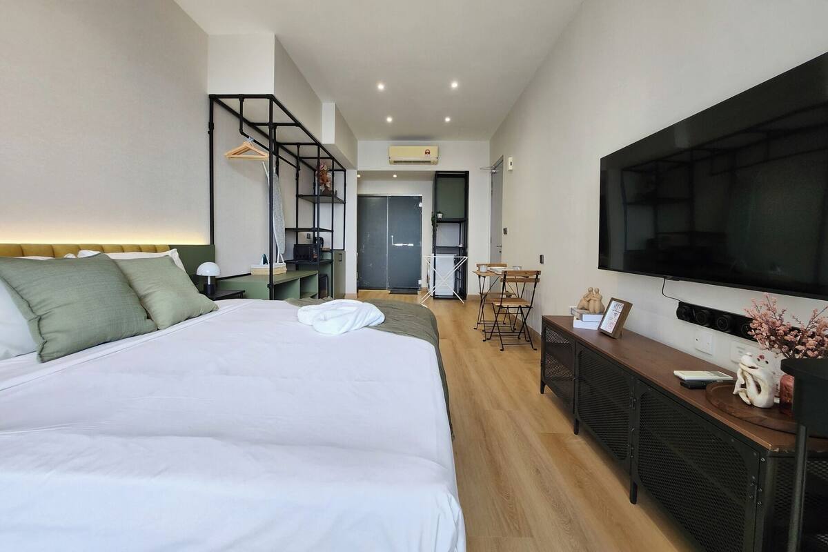 A modern hotel room with a large bed, a TV, a desk, and a seating area.