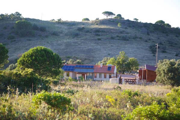 A house with solar panels on the roof, surrounded by greenery and hills. - Biovilla Sustentabilidade (Palmela)