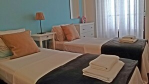 A hotel room with two beds, a bedside table with a lamp, a dresser, and a window with curtains. - TripGeo Apartment Roma (Lisbon)