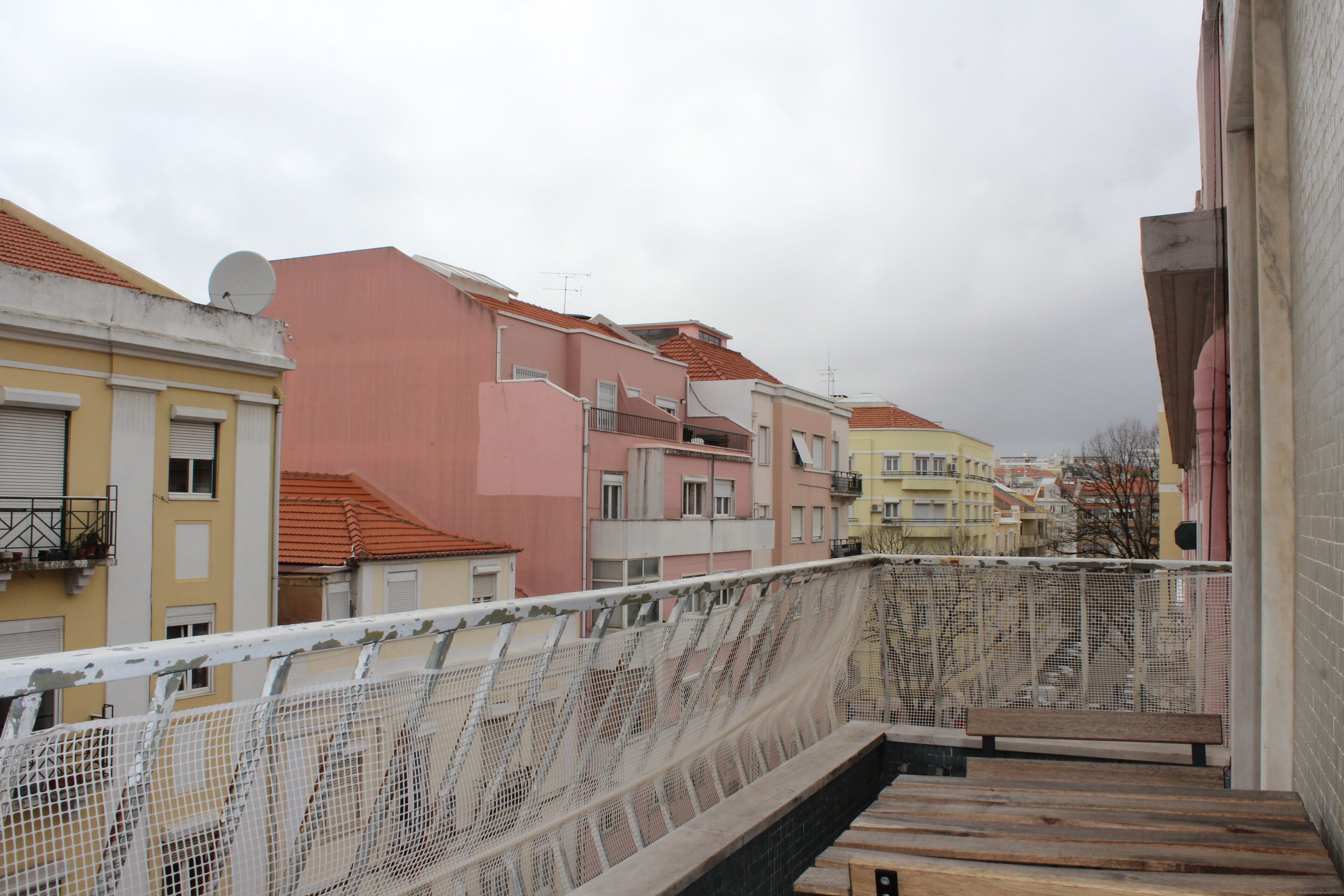 A balcony with a white mesh railing overlooking a row of colorful buildings.