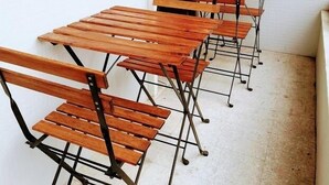 A row of wooden desks with metal frames, arranged in a narrow corridor with white walls and a window with blinds. - TripGeo Apartment Roma (Lisbon)