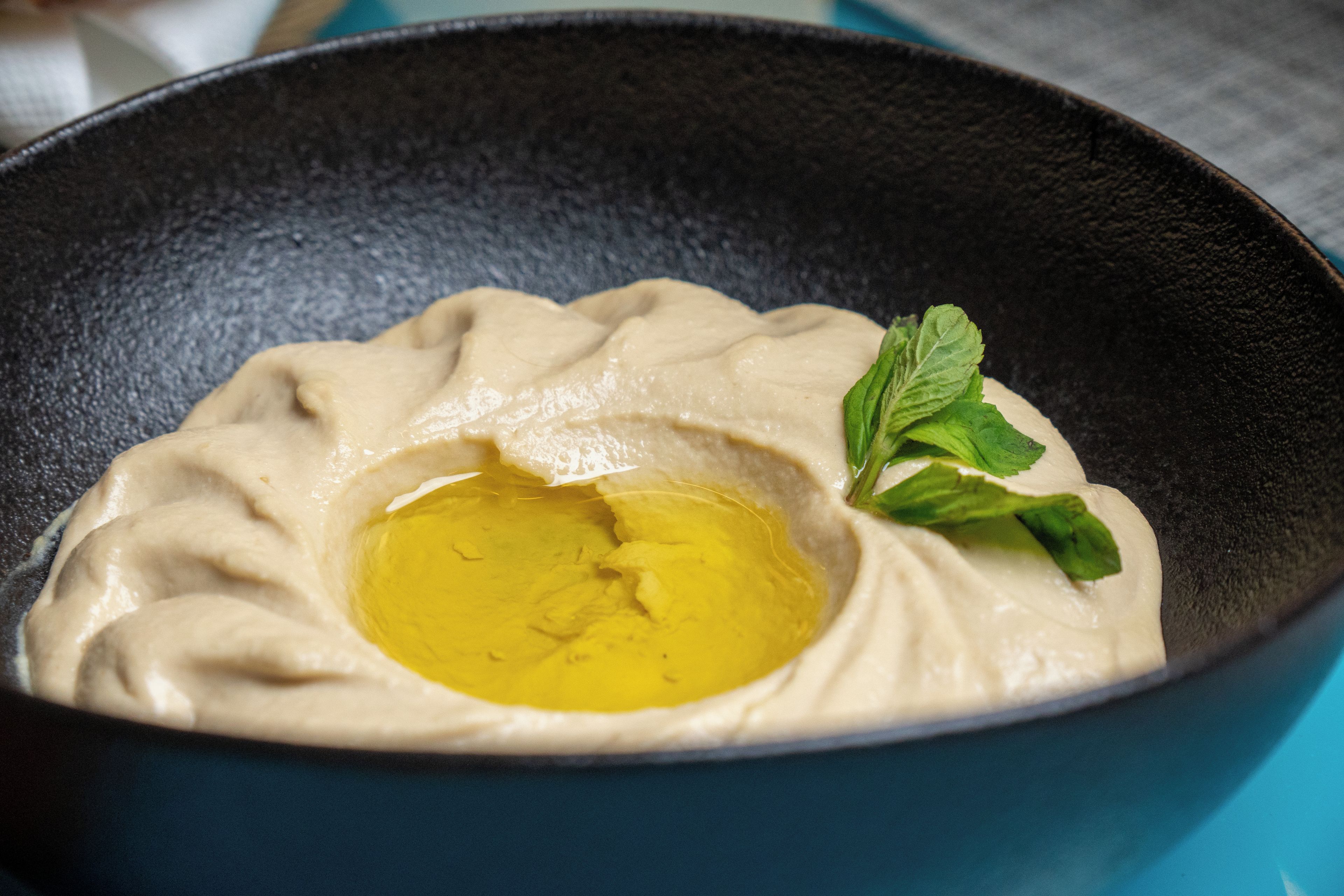 A bowl of hummus with olive oil and a mint leaf garnish.