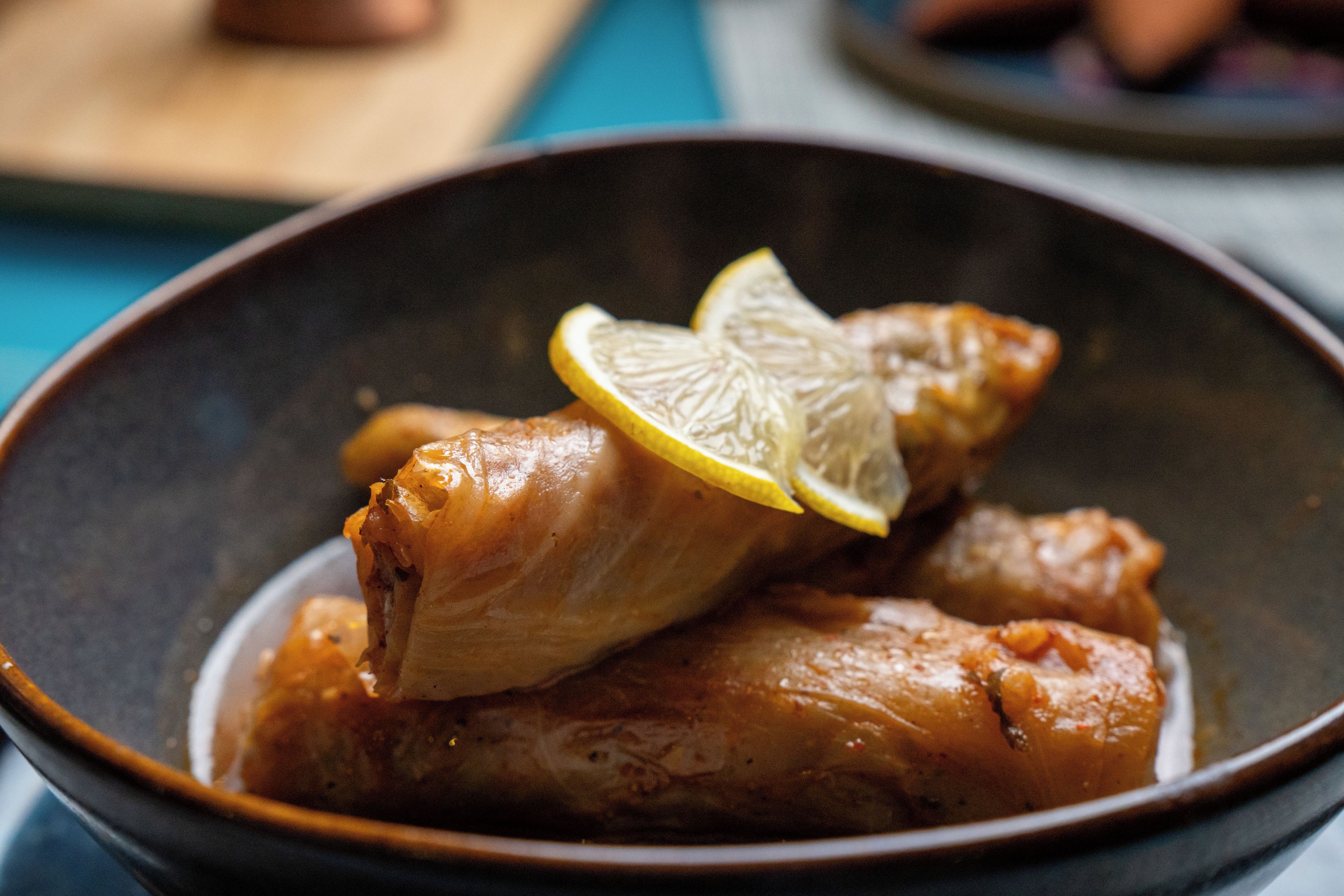 A bowl containing two pieces of stuffed cabbage rolls garnished with a slice of lemon.