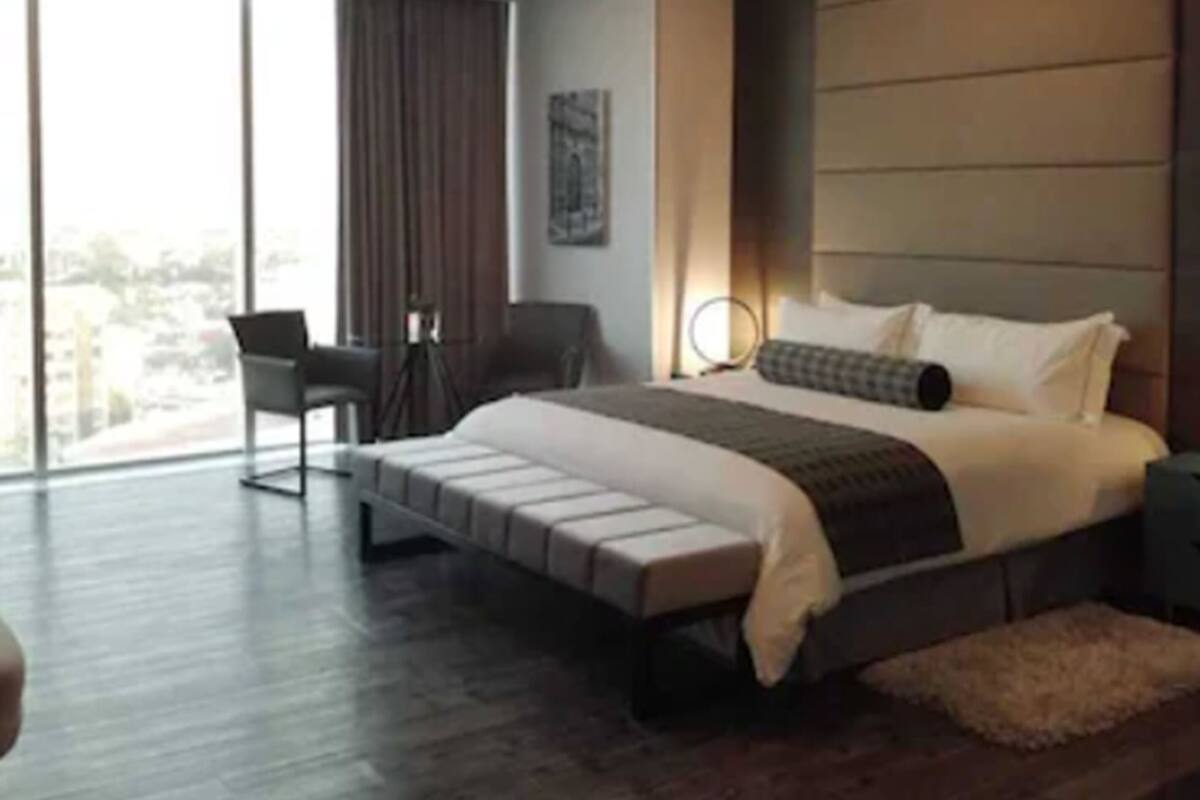 Ein modernes Hotelzimmer mit einem großen Bett, einem Schreibtisch und einem Sessel. Ein großes Fenster bietet Blick auf die Stadt.