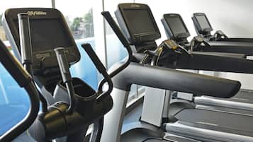 A gym with stationary bikes and treadmills, large windows, and a ceiling-mounted light fixture.