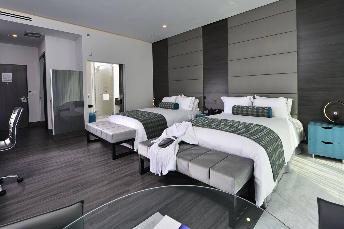 Ein modernes Hotelzimmer mit zwei Betten, einem Schreibtisch, einem Stuhl und einem durch eine offene Tür einsehbarer Badezimmer.