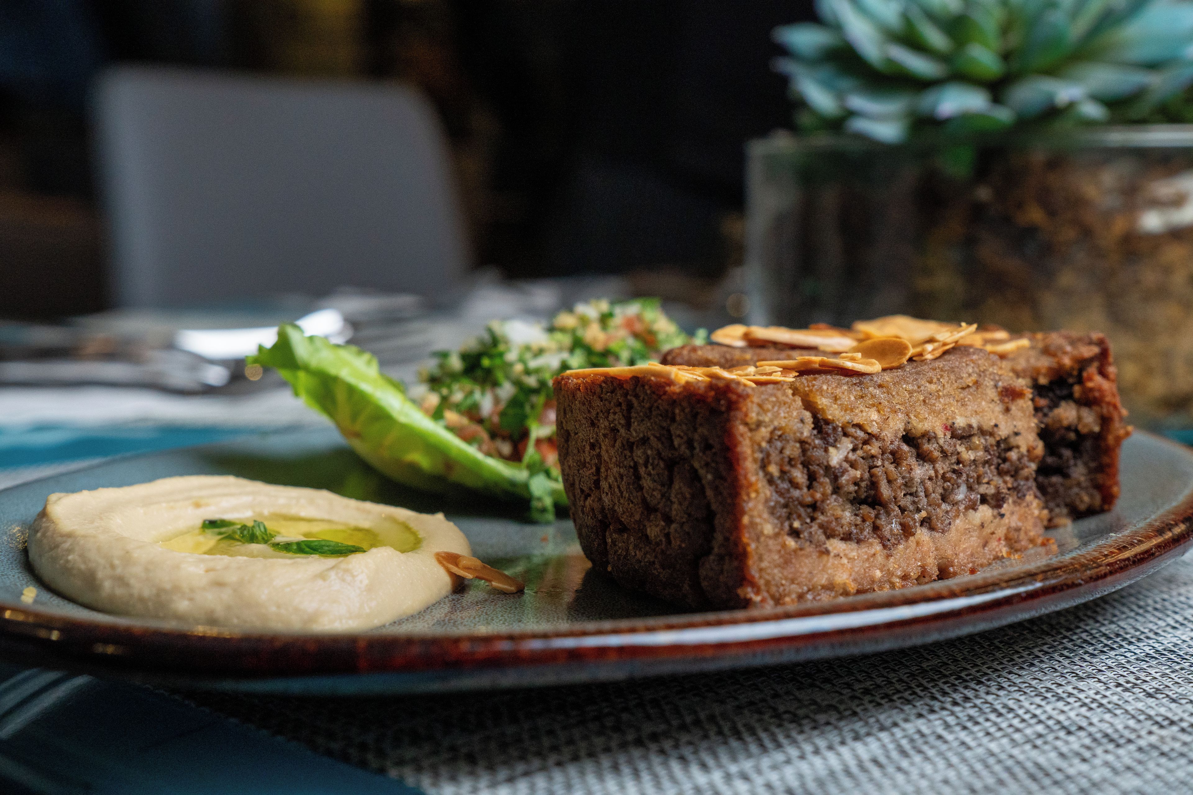 A plate with a slice of meatloaf, a dollop of hummus, and a side salad.