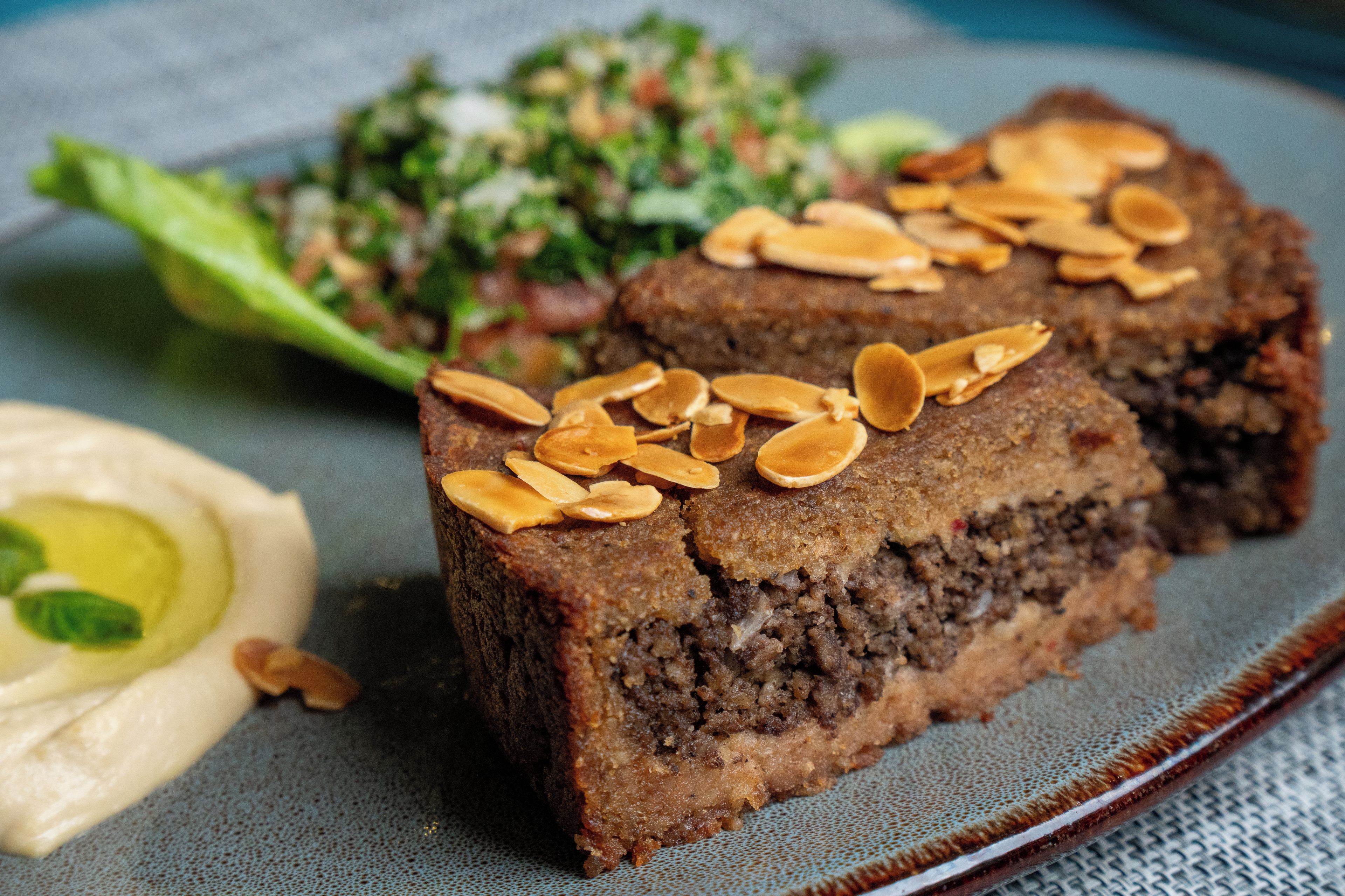 Een bord met een plakje cake, bestrooid met amandelen, een portie hummus en een salade.