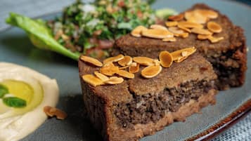 A plate with a slice of cake topped with almonds, a side of hummus, and a salad.