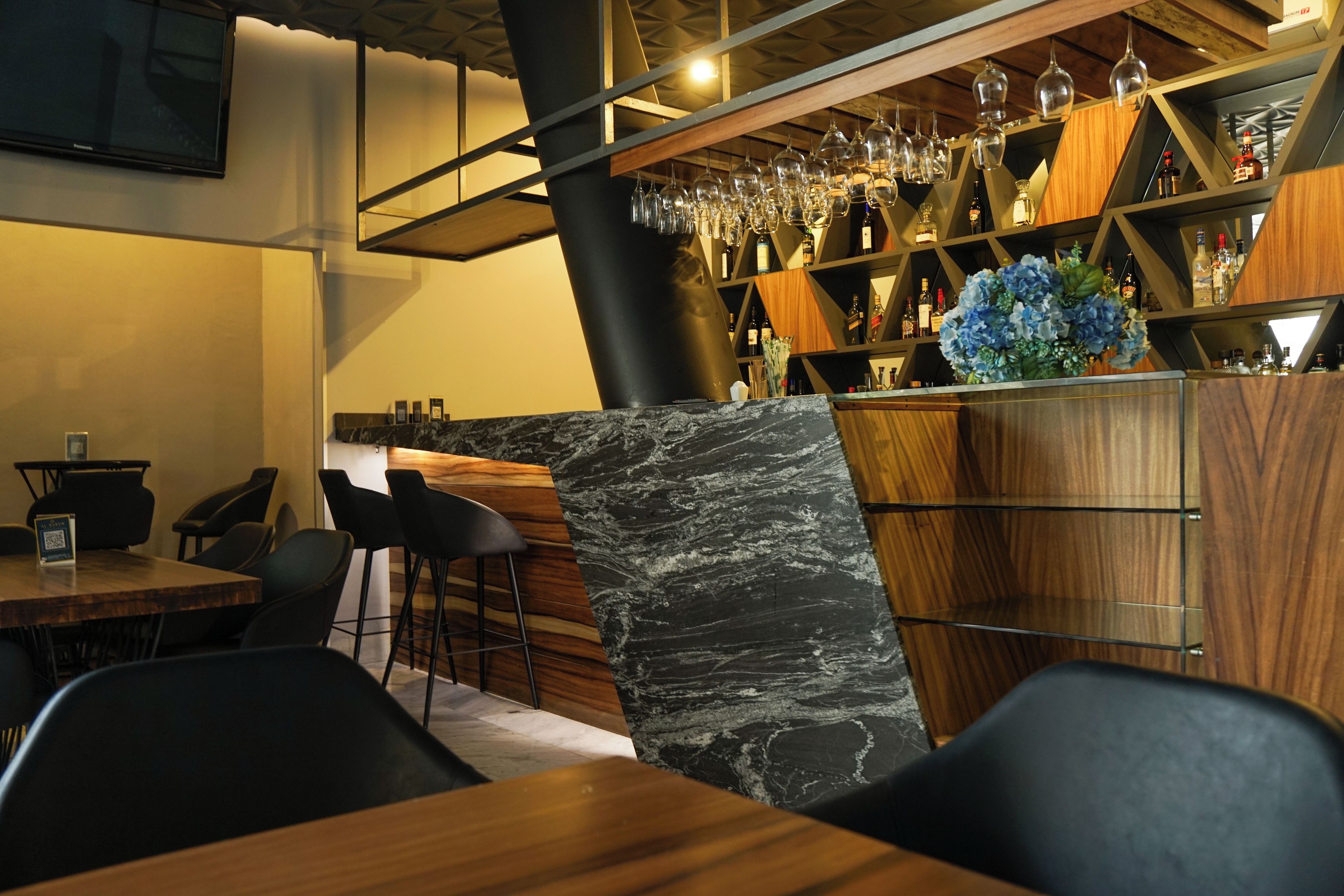 A bar area with a marble countertop, bar stools, and a variety of bottles and glasses.