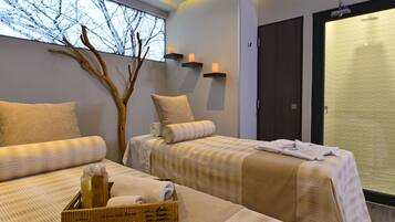 Two beds with striped bedspreads and pillows, a wooden tree branch, and a wooden tray with amenities.