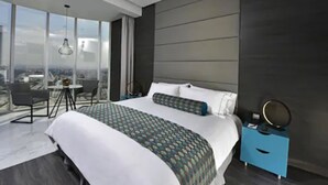 A modern hotel room with a large bed, a small desk, and a view of the city.