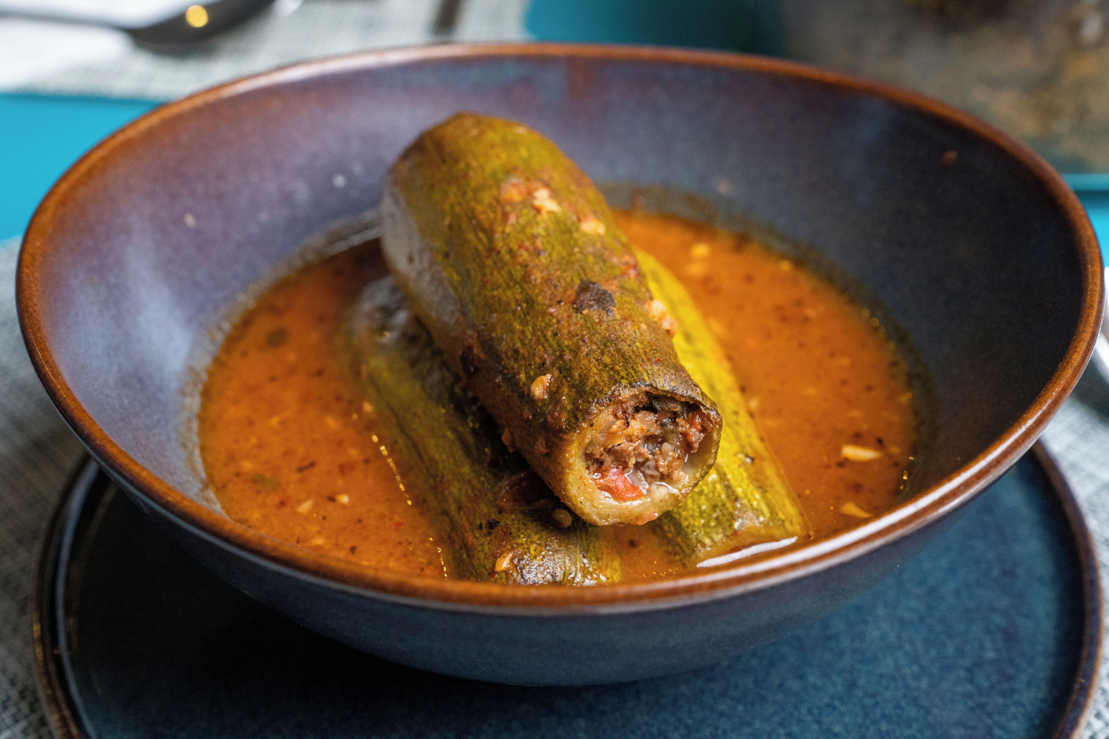 A bowl of stuffed zucchini with a sauce, placed on a blue surface.
