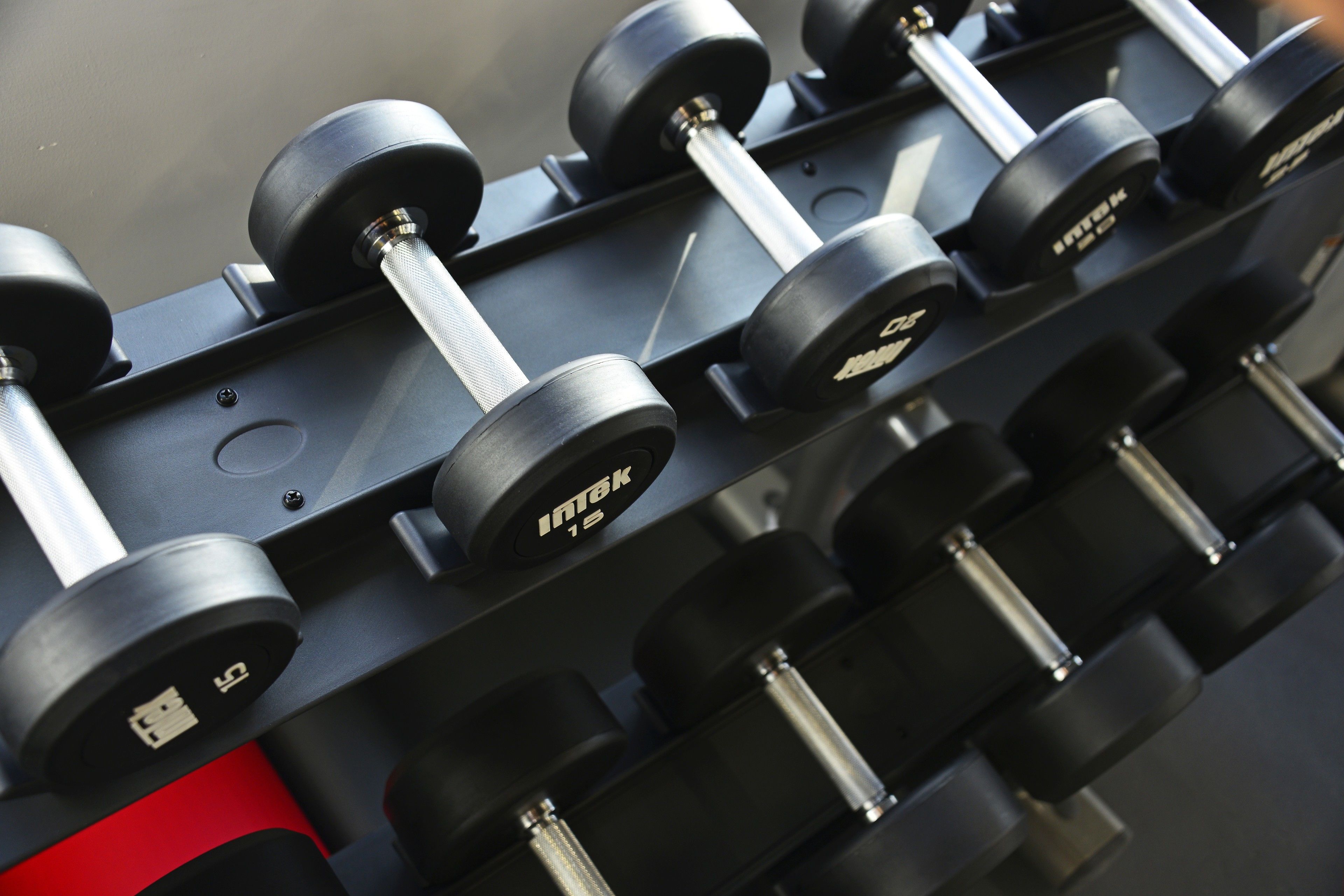 A set of black dumbbells with the brand name "INTEK" on them, arranged on a rack.
