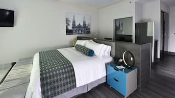 Une chambre d’hôtel avec un lit, une table de chevet avec un téléphone et une lampe, un miroir et un tableau représentant un bâtiment accroché au mur.