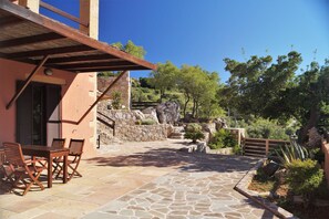 A stone patio with outdoor furniture, a stone wall, and a view of a hillside with trees.