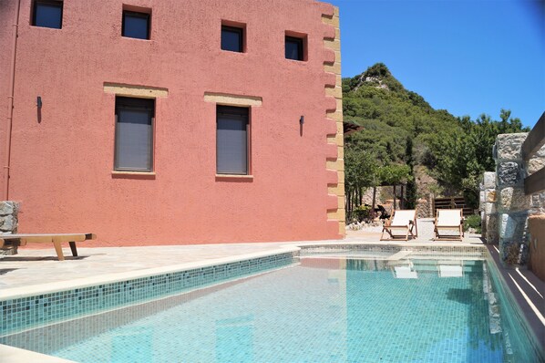 A pool area with a red building, two windows, and a stone wall.