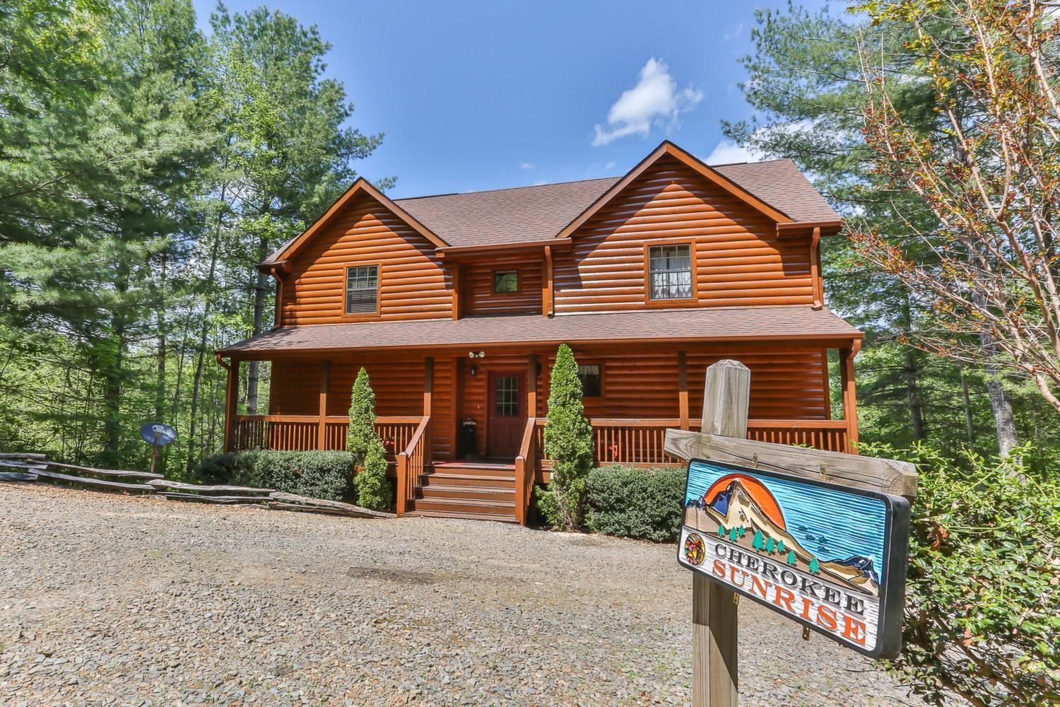 A two-story log cabin with a porch, surrounded by trees.