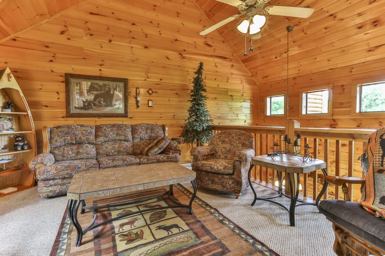 L’intérieur d’un chalet chaleureux, avec un plafond en bois, un grand canapé, un fauteuil plus petit, une table basse et un sapin de Noël.