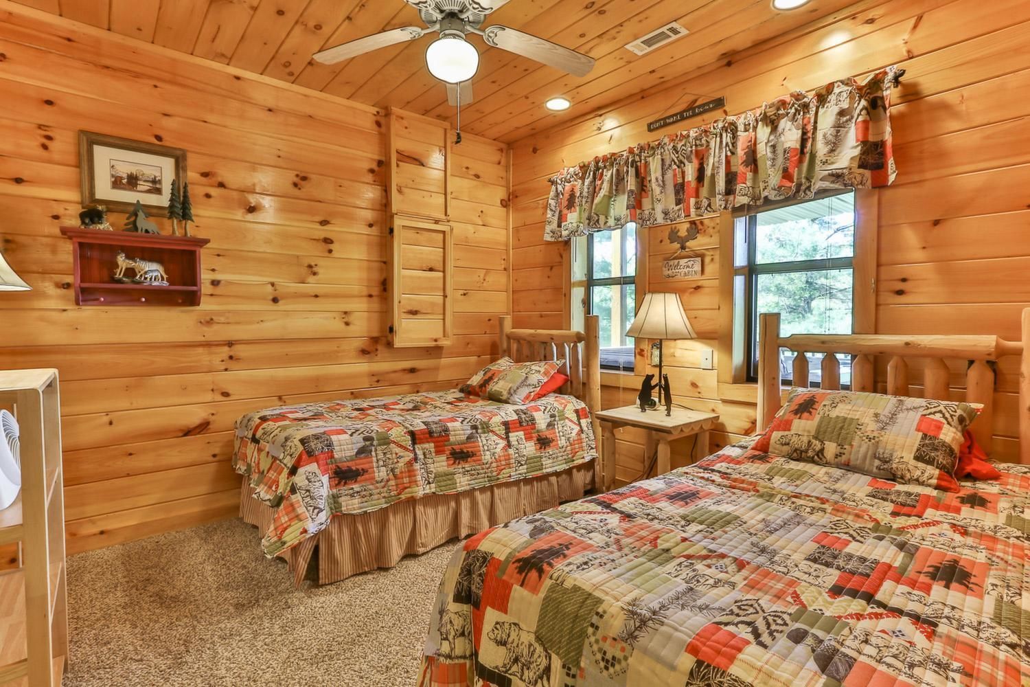 A cozy cabin room with two beds, a ceiling fan, and a window with curtains.
