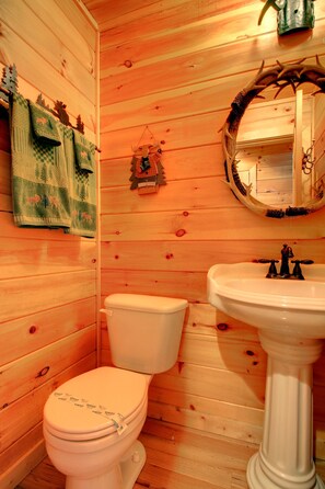 Ein Badezimmer mit Holzwänden, einer Toilette, einem Waschbecken und Dekorationselementen.