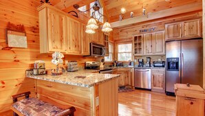 A wooden cabin kitchen with granite countertops, a central island, a refrigerator, and a microwave. - Crockett Mountain Lodge Nevaeh Cabin Rentals (Blue Ridge)