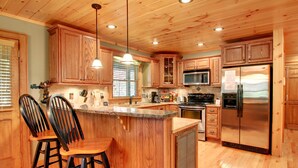 A kitchen with wooden cabinets, a stainless steel refrigerator, and a bar area with stools. - SERENITY WOODS Apartment 3 NEVAEH CABIN RENTALS (Mineral Bluff)