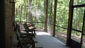 A covered outdoor seating area with benches and large windows offering a view of a forest. - SERENITY WOODS Apartment 3 NEVAEH CABIN RENTALS (Mineral Bluff)