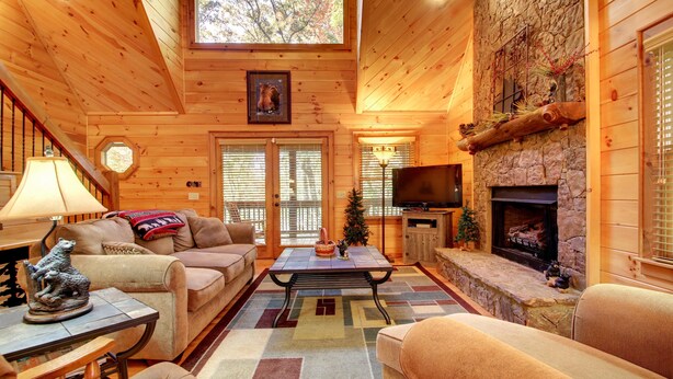 A cozy log cabin interior with a fireplace, wooden walls, a sofa, a coffee table, and a television. - SERENITY WOODS Apartment 3 NEVAEH CABIN RENTALS (Mineral Bluff)