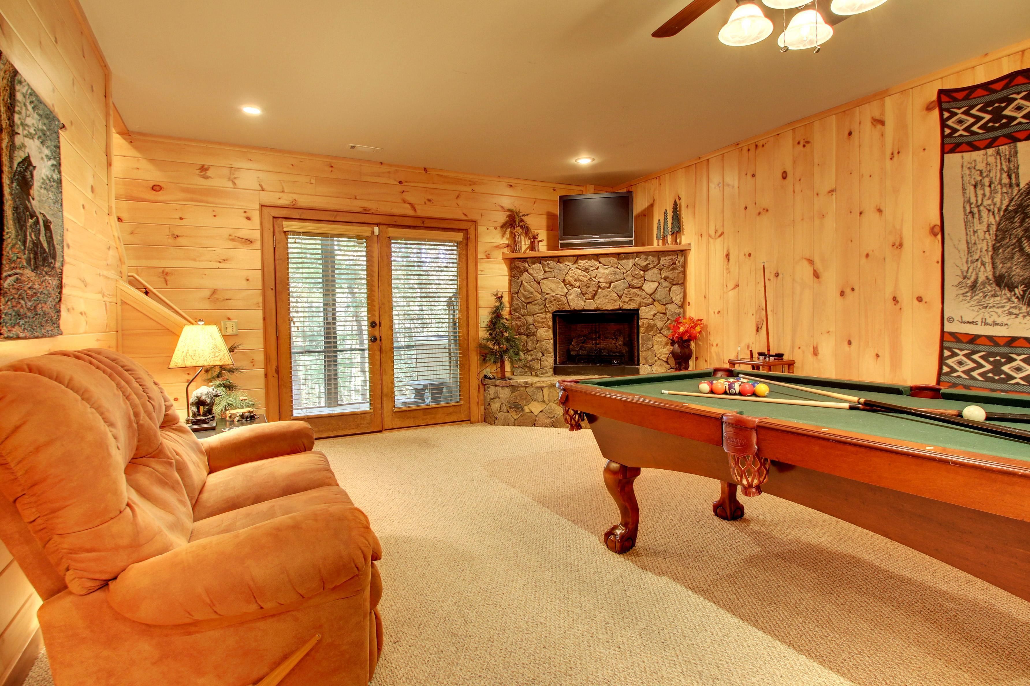 A cozy room with a pool table, a comfortable armchair, and a stone fireplace.