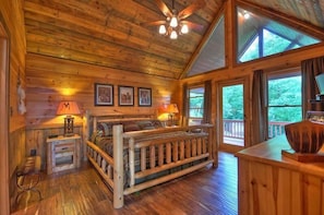 A wooden cabin bedroom with a bed, two nightstands, a ceiling fan, and large windows. - Wild Things Nevaeh Cabin Rentals (Blue Ridge)