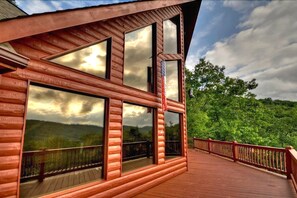 A wooden cabin with large windows and a deck overlooking a forested landscape. - Wild Things Nevaeh Cabin Rentals (Blue Ridge)