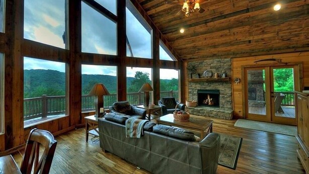 Un salón amplio con chimenea de piedra, ventanas grandes y techo de madera.