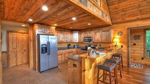 Una cocina rústica con gabinetes de madera, un refrigerador de acero inoxidable, un microondas y una zona de bar con taburetes.