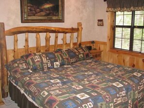 Ein rustikales hölzernes Bett mit einer gesteppten Bettdecke, einem Holz-Kopfteil, einem Nachttisch und einem Fenster mit Jalousien.