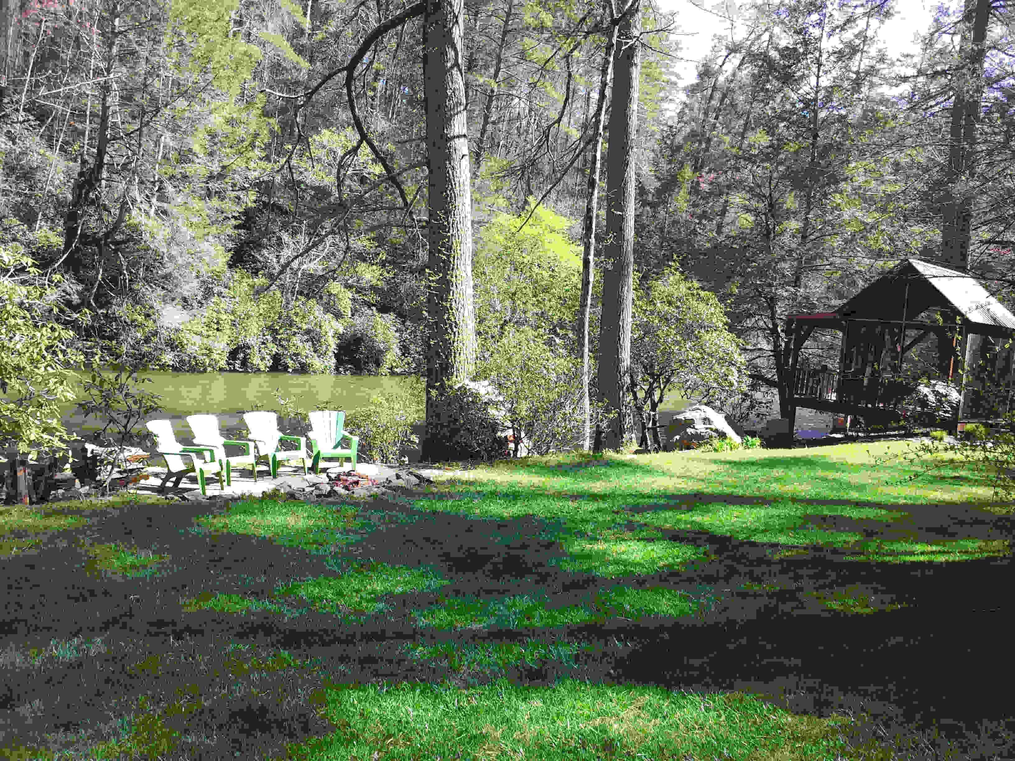 A forested area with a gazebo and two green chairs near a pond.