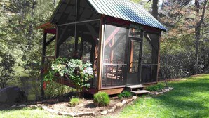 A small wooden cabin with a metal roof, surrounded by a garden and a pond. - Pick's Riverside Retreat Nevaeh Cabin Rentals (Blue Ridge)