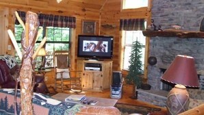 A cozy cabin interior with a television, wooden furniture, and a stone fireplace. - Pick's Riverside Retreat Nevaeh Cabin Rentals (Blue Ridge)