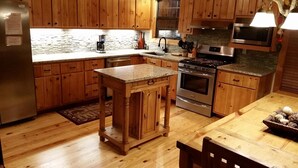 A kitchen with wooden cabinets, a granite countertop, stainless steel appliances, and a wooden dining table. - Pick's Riverside Retreat Nevaeh Cabin Rentals (Blue Ridge)