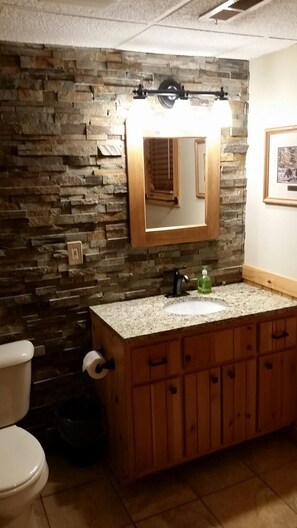 Ein Badezimmer mit Steinwand, Waschtisch aus Holz, Waschbecken und Toilette.