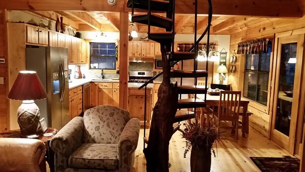A cozy cabin interior with a dining area, kitchen, and a spiral staircase. - Pick's Riverside Retreat Nevaeh Cabin Rentals (Blue Ridge)