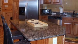 Uma cozinha com armários de madeira, geladeira de aço inoxidável, micro-ondas e bancada de granito.