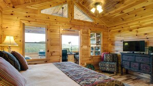A log cabin bedroom with a bed, a TV, a desk, and a chair.