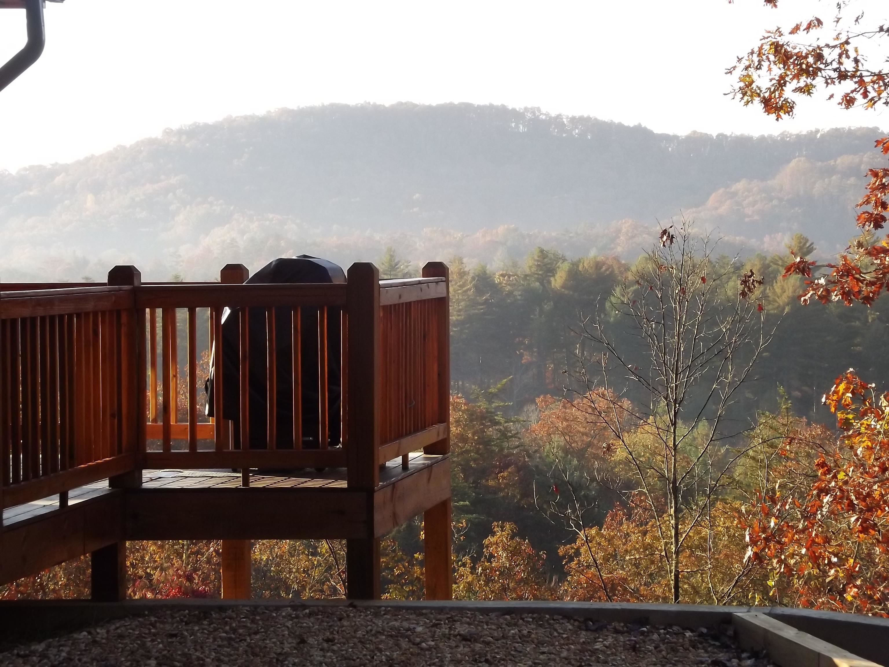 A wooden deck with a bench overlooking a forested hillside.