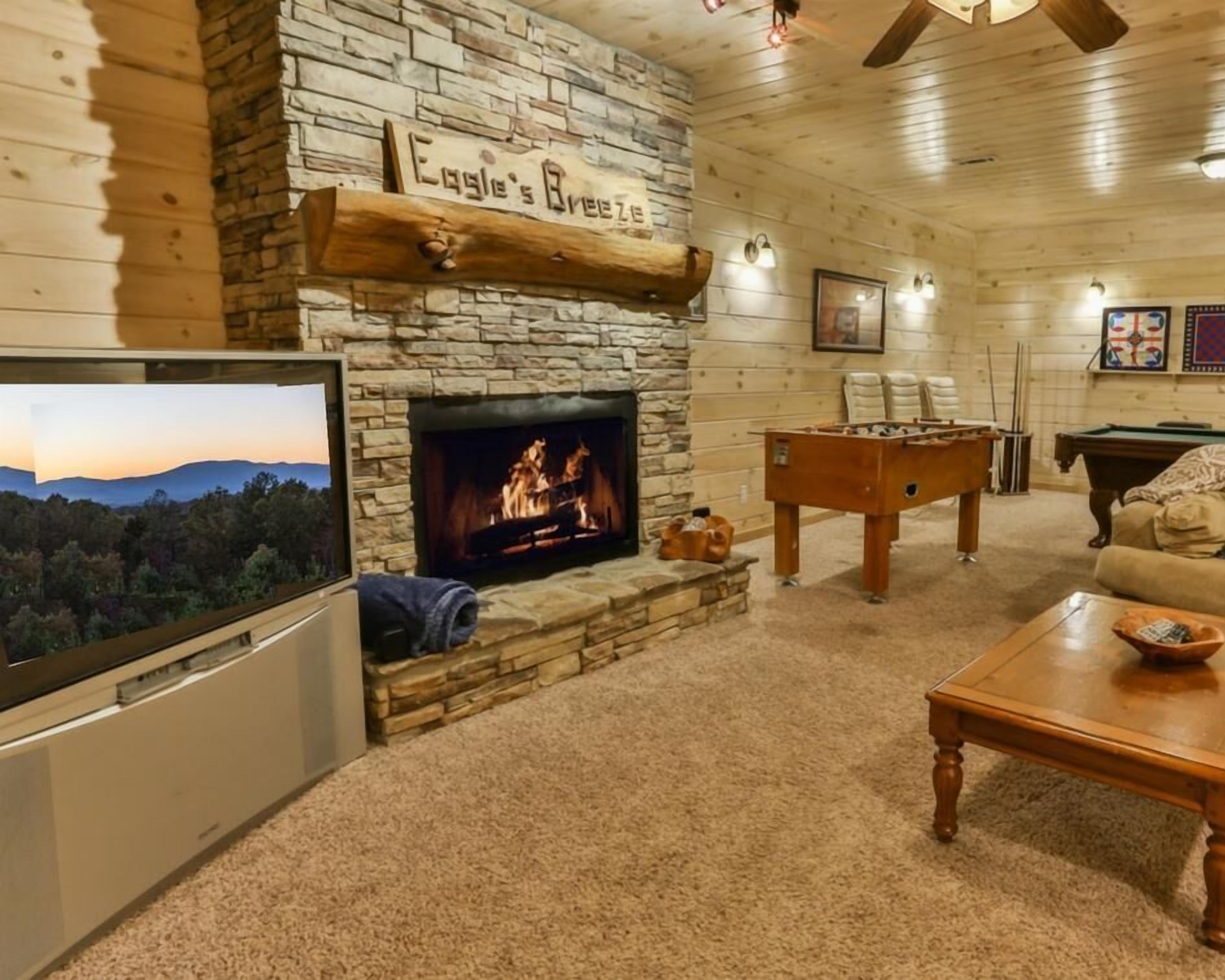 A cozy living room with a stone fireplace, a pool table, and a television.