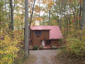 A cabin with a red roof, surrounded by trees with autumn foliage.