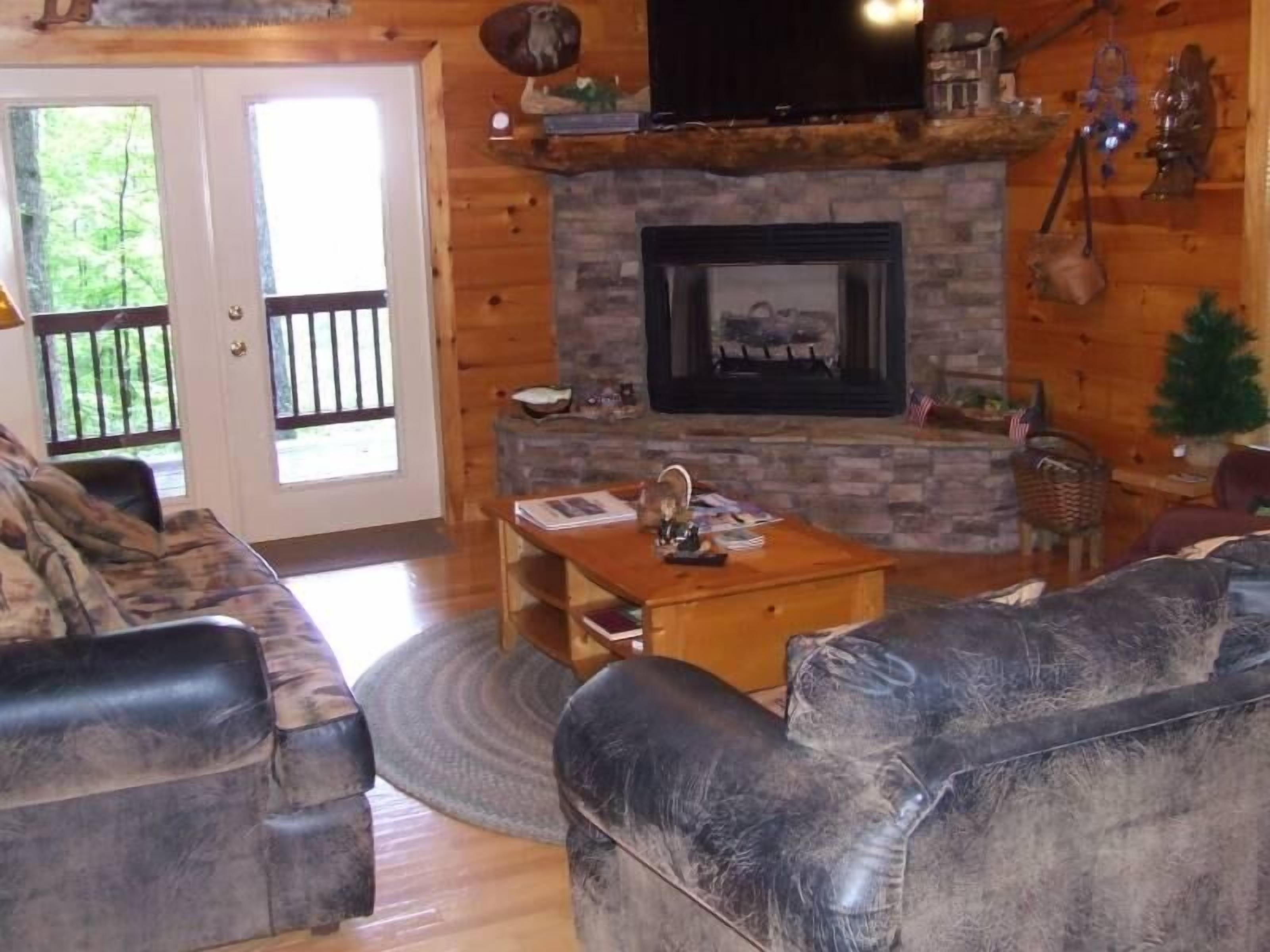 A cozy living room with a stone fireplace, leather sofas, and a television.