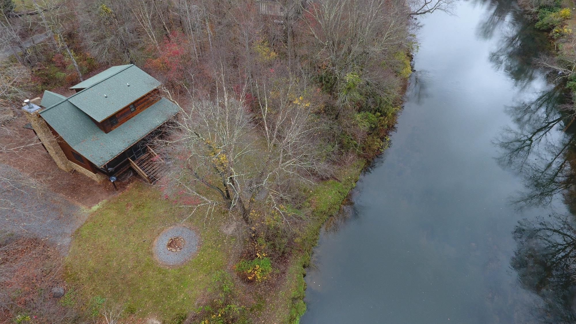 A cabin with a green roof, surrounded by trees and a body of water.